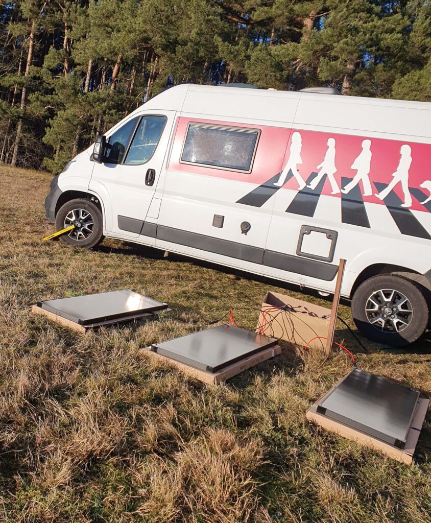 Camper Elektrik Test auf dem Feld vor dem finalen Einbau, Solarpanels liegen noch am Boden und werden angeschlossen.