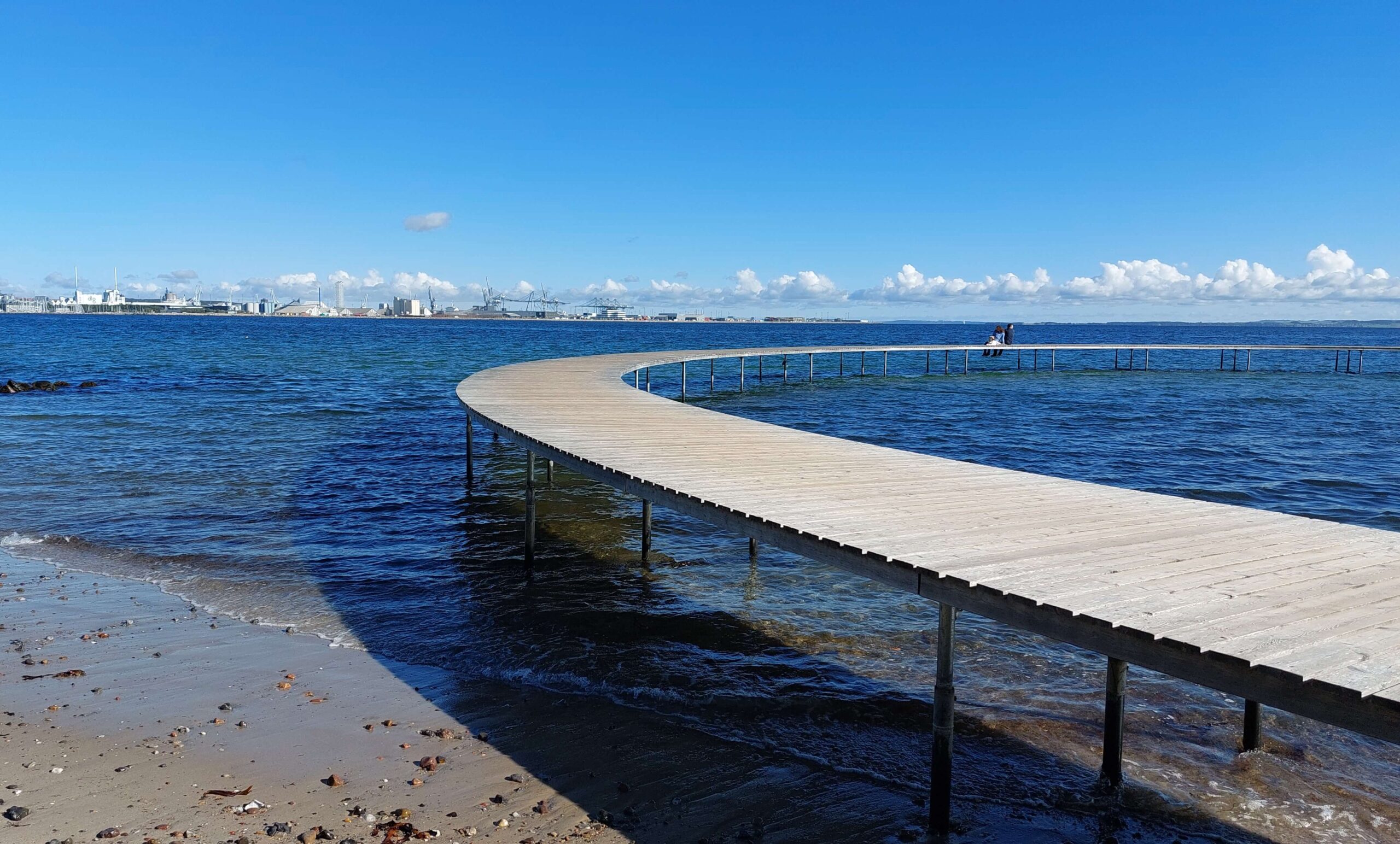 Steg am Meer als Symbol für Reisen mit Camper und Hund In Europa und das Gefühl von Freiheit. Zu sehen ist ein runder Steg aus Holz am Strand über den Meer. Es scheint die Sonne.