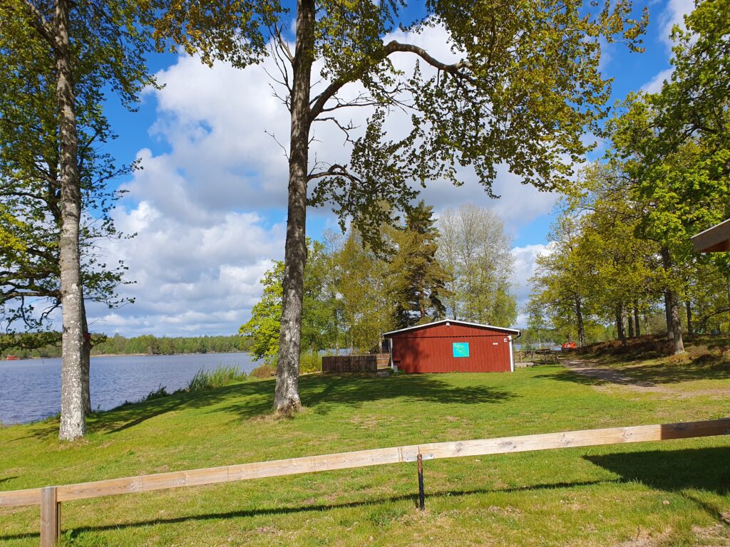 Haus am See in Schweden entdeckt beim Wandern. Bäume See und ein rotes haus sind zusehen im Bild. es scheint die Sonne.