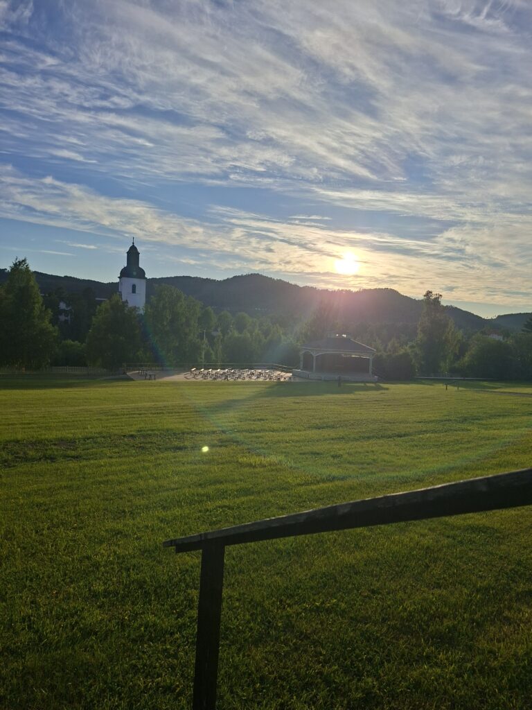 Kirche in Järvsö in Schweden unterwegs mit Camper. Die Sonne scheint und es ist im Vordergrund eine große Rassenfläche zu sehen.