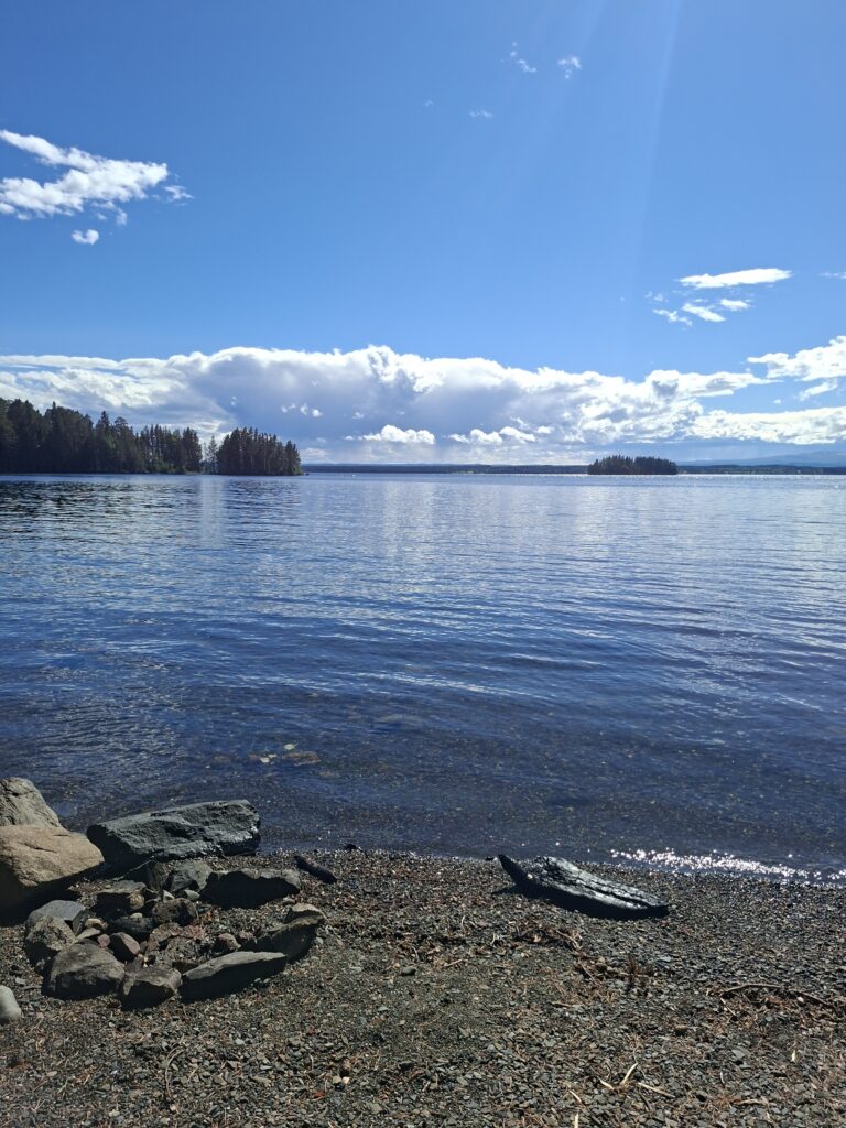 Ruhiger See in Schweden mit kleinen bewaldeten Inseln, sanften Wellen und blauem Himmel mit weißen Wolken.