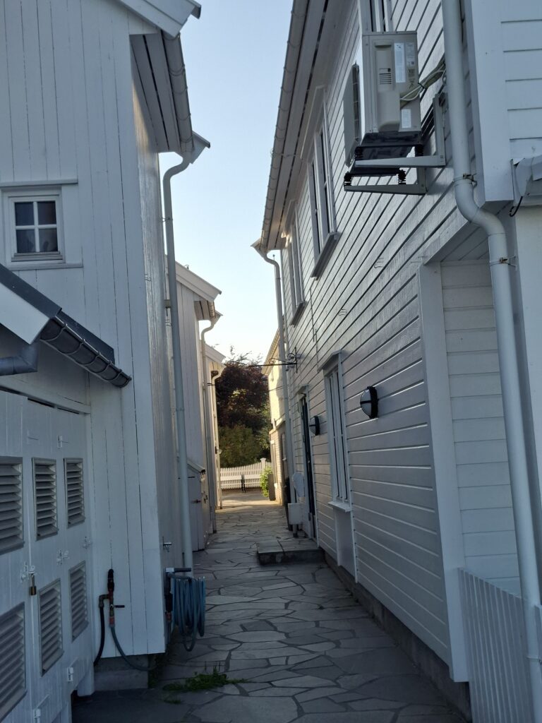 Schmale Gasse zwischen den typischen weißen Holzhäusern in Lillesand an der Südküste Norwegens. Weiß gestrichene Häuser.