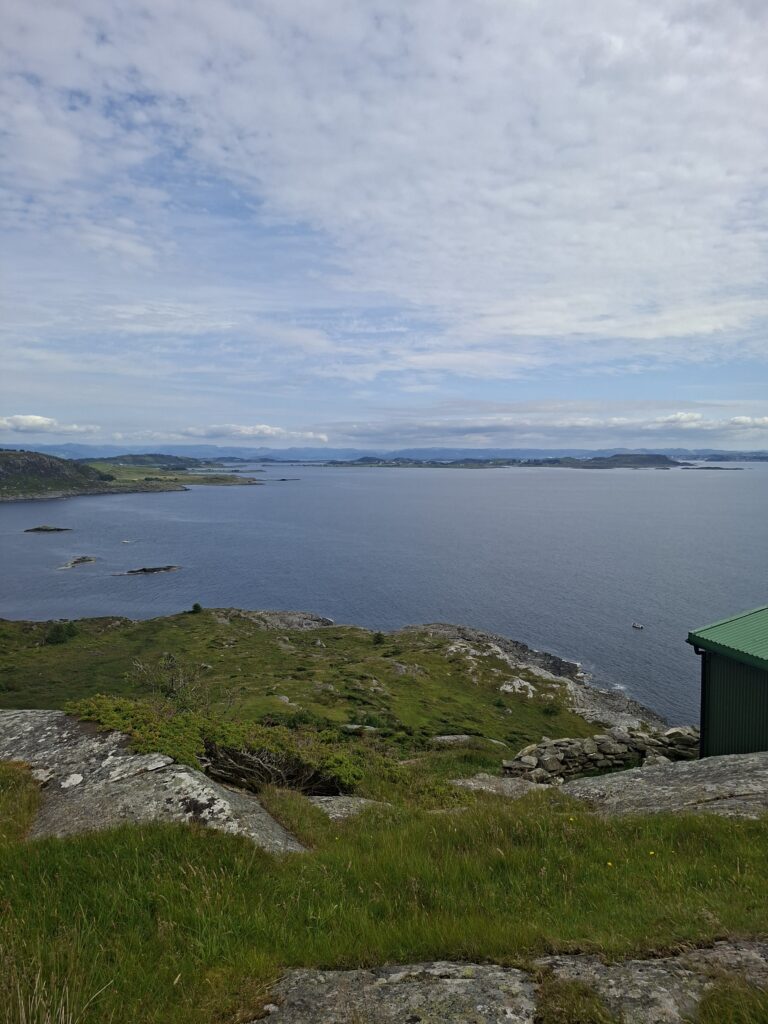 Panoramablick über die felsige Küstenlandschaft von Fjøløy mit grasbewachsenen Felsen, kleinen Inseln und ruhigem Meer. Dieser Aussichtspunkt gehört für uns zu den schönsten Orten in Norwegen mit dem Camper.