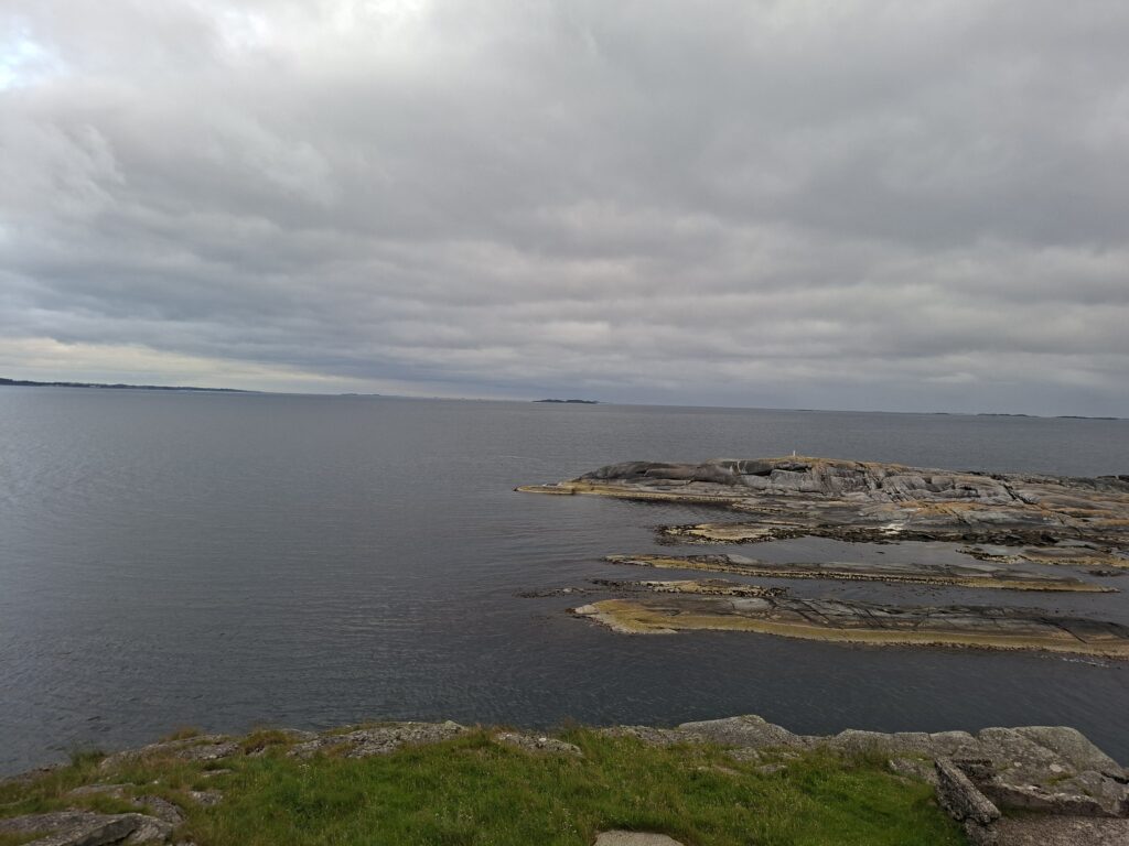Weitläufiger Blick über die Küstenlandschaft von Fjøløy mit felsigen Inseln, ruhigem Meer und bewölktem Himmel. Von hier oben bietet sich eine beeindruckende Aussicht auf die norwegische Küste.