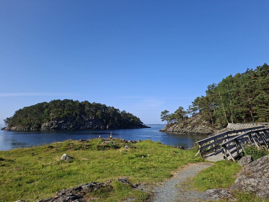 Blick über die kleine Bucht im Erikane Friluftsområde mit glasklarem Wasser, bewaldeten Inseln und einer Holzbrücke am Ufer. Dieser ruhige Naturort gehört für uns zu den schönsten Orten in Norwegen mit dem Camper.