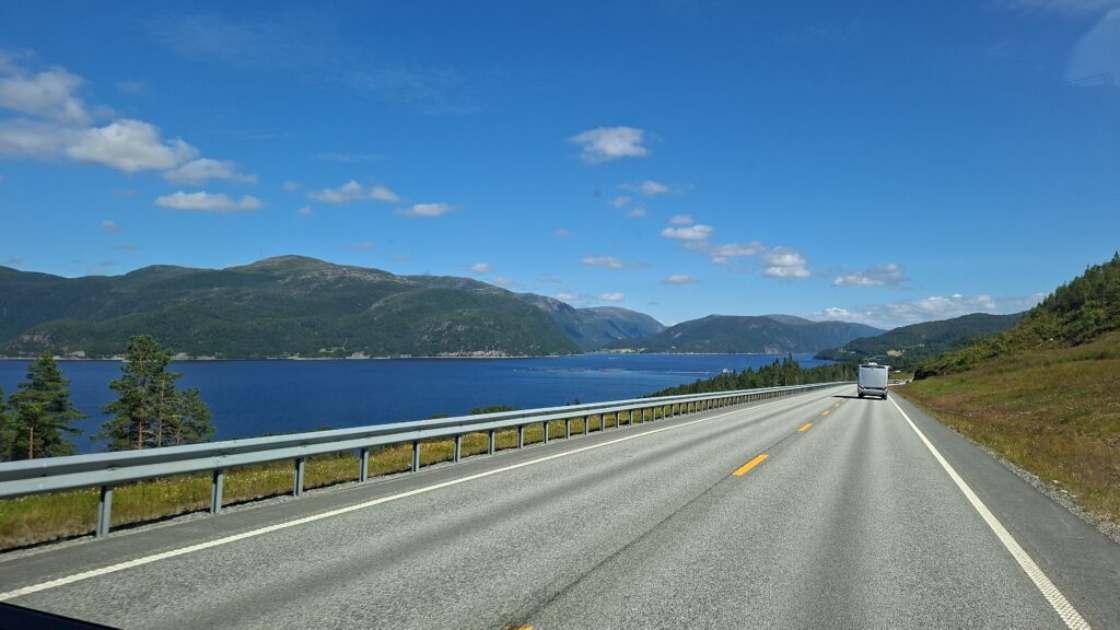 Camper fährt auf einer Küsten Straße durch Norwegen mit Blick auf Fjorde und berge. Unterwegs zu den schönsten Orten in Norwegen.