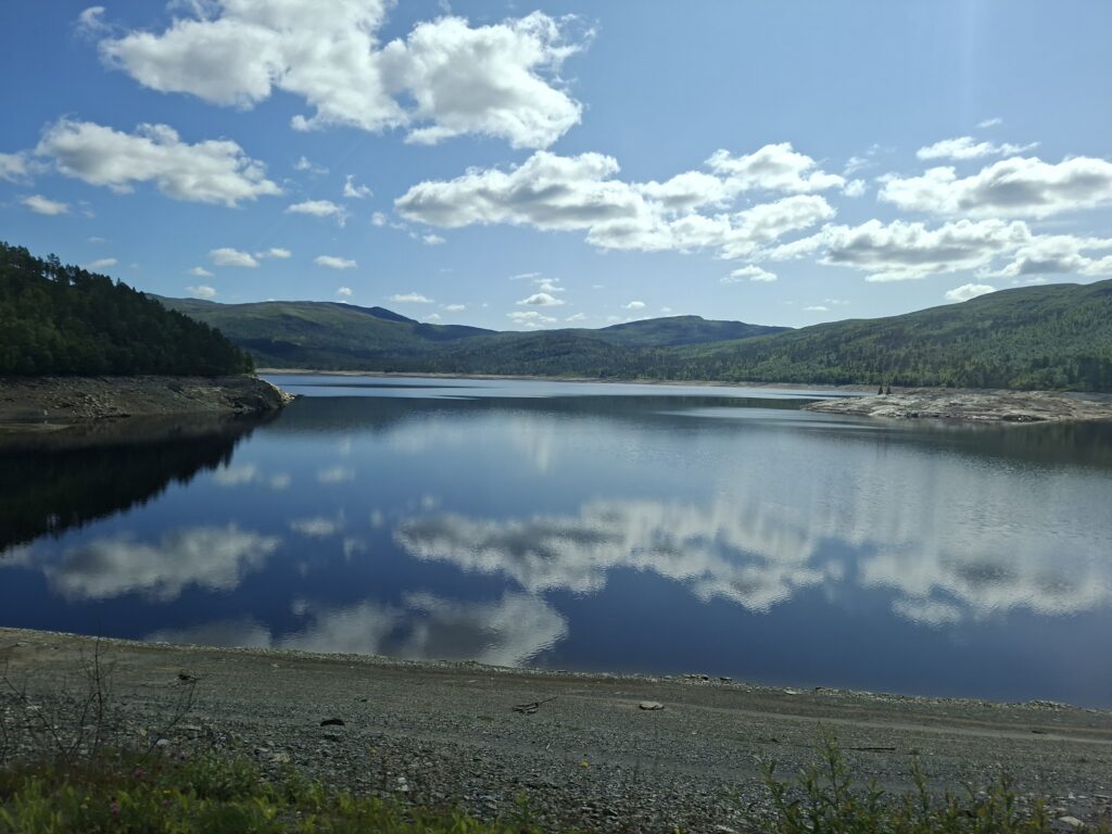 Ruhiger See in Norwegen mit spiegelnder Wasseroberfläche und bewaldeten Hügeln im Hintergrund. Die friedliche Stimmung machte diesen Ort zu einem besonderen Zwischenstopp.