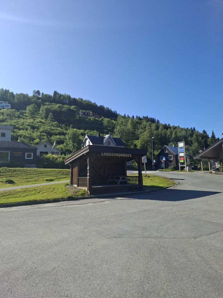 Ortseingang von Løkken Verk mit Bushaltestelle, Holzhäusern und bewaldetem Hang im Hintergrund. Der ehemalige Bergbauort hat uns mit seiner Geschichte und den schönen Wanderwegen positiv überrascht.