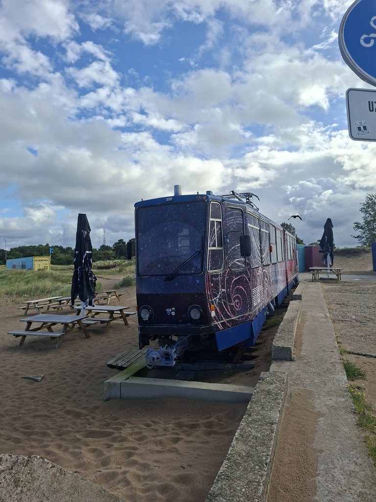 Alte Tram in Lettland am Strand. Es ist ein Kaffee heute. Bund besprühte Tram im Sandstrand am Meer.